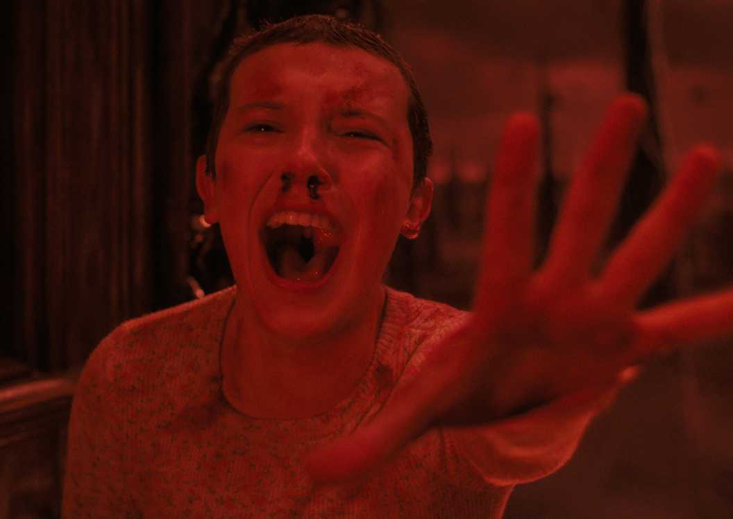 Eleven screaming and reaching out in the Upside Down in red light in Stranger Things season 4
