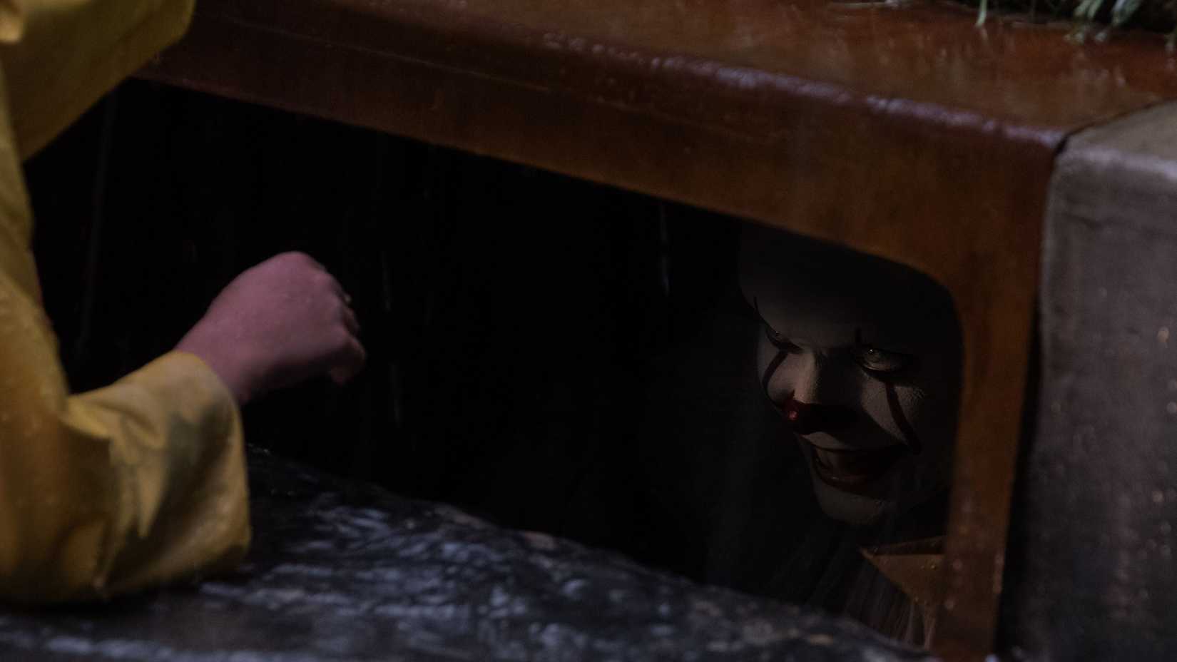 Georgie (Jackson Robert Scott) reaching into the sewer while Pennywise (Bill Skarsgård) watches and smiles in It.