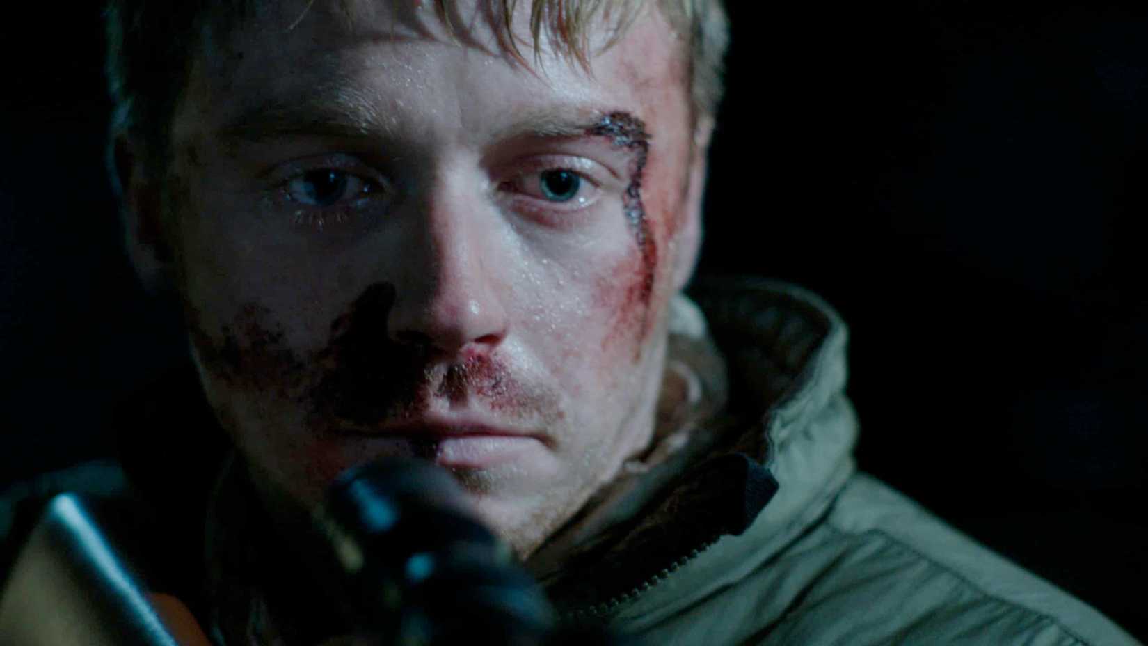 Jack Lowden as Vaughn bleed and holding a rifle in Calibre