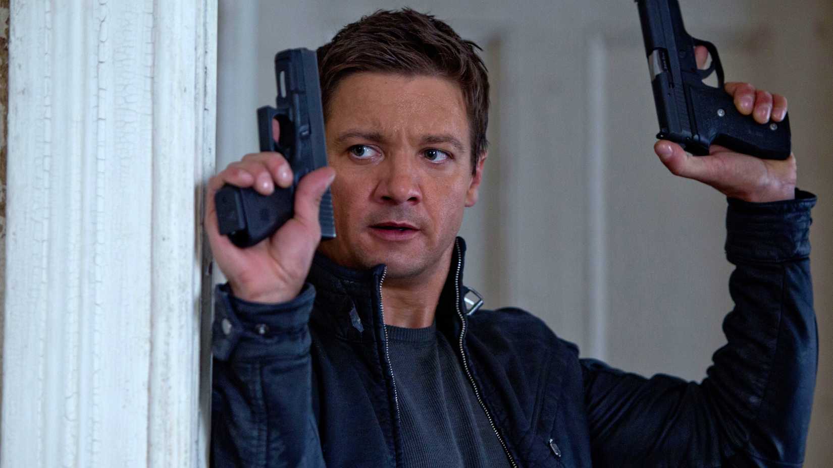 Jeremy Renner as Aaron Cross holding up two guns in The Bourne Legacy