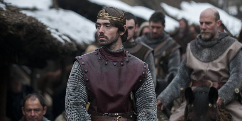 King Alfred looks to the side with other men standing behind him in The Last Kingdom