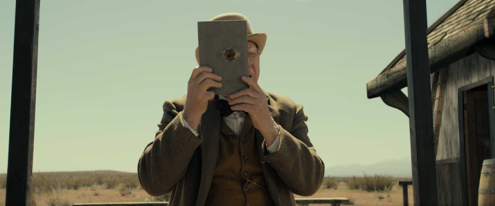 Malcolm McDowell looks through a bullet hole shoes through a book in Last Train to Fortune