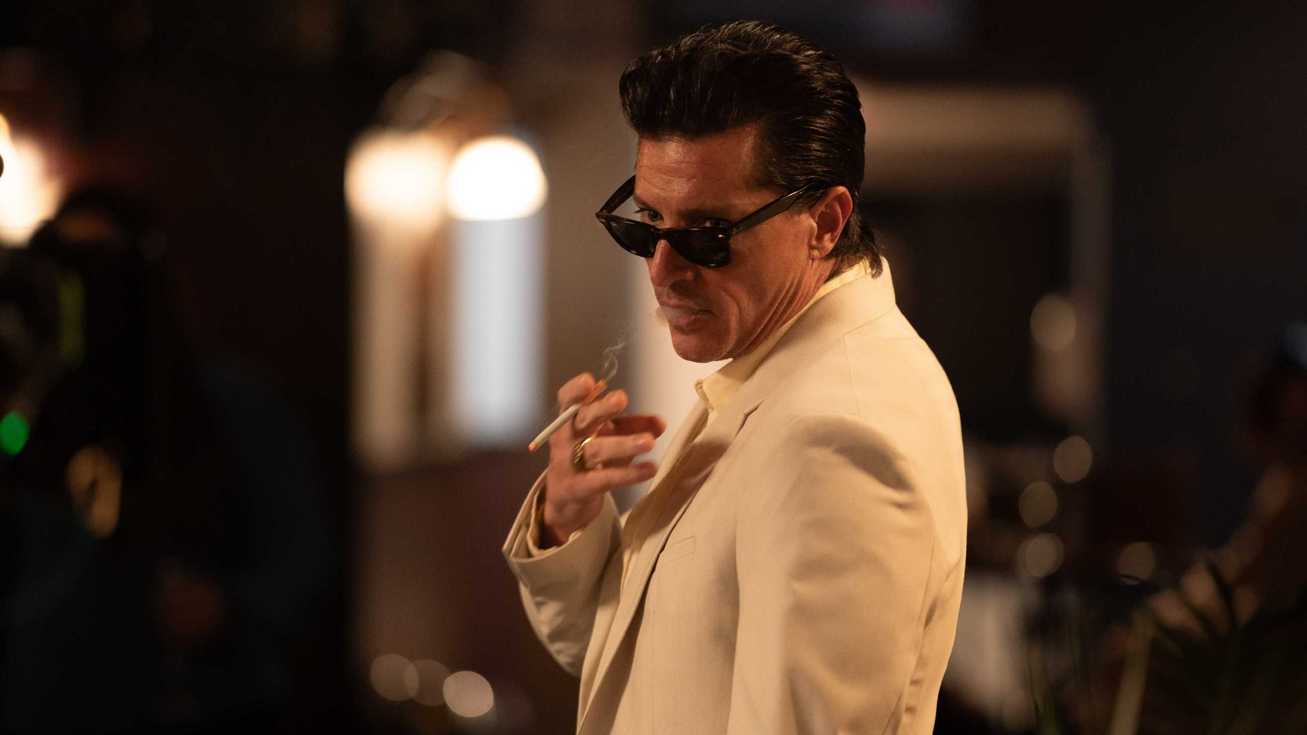Marco in a white suit and sunglasses smoking a cigarette in God Bless You, Mr. Kopu
