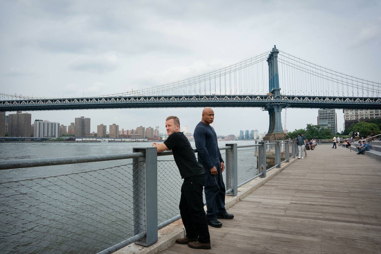 Sam Hanna and Nick Schaeffer standing on a walkway next to a river, one of New York's bridges behind them.