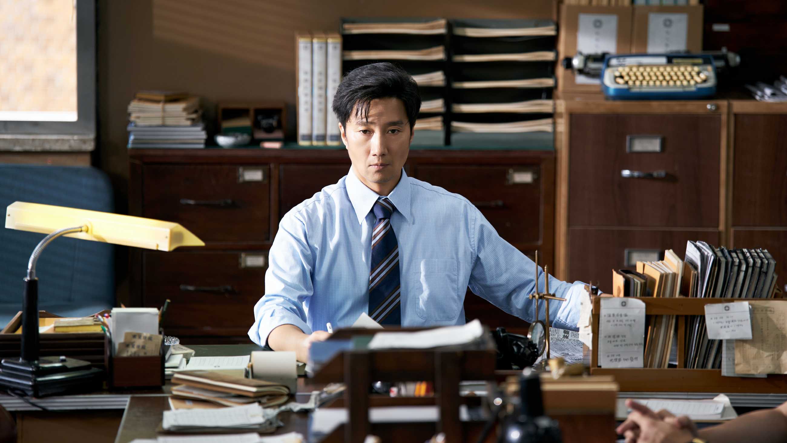 Park Hae-il sitting at his desk in The Assassin(s)