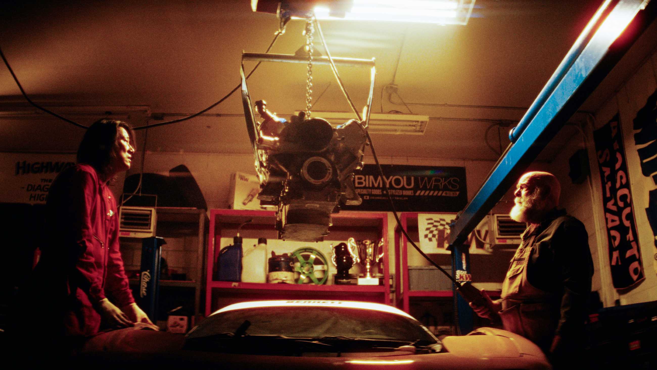Sung Kang and a mechanic face each other as an engine is lowered into a car in Drifter