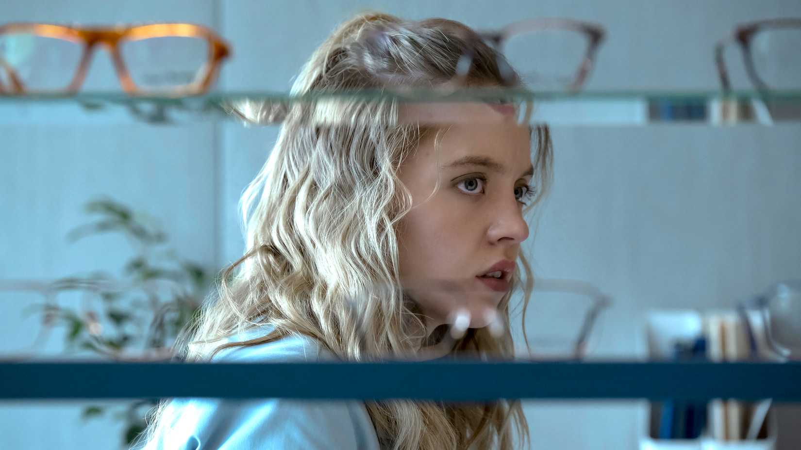 Sydney Sweeney's Pippa looking worried behind shelves with glasses on it in The Voyeurs