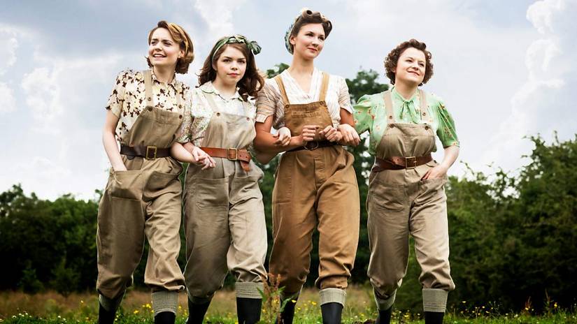 The four women of Land Girls walking through a field, arm-in-arm.