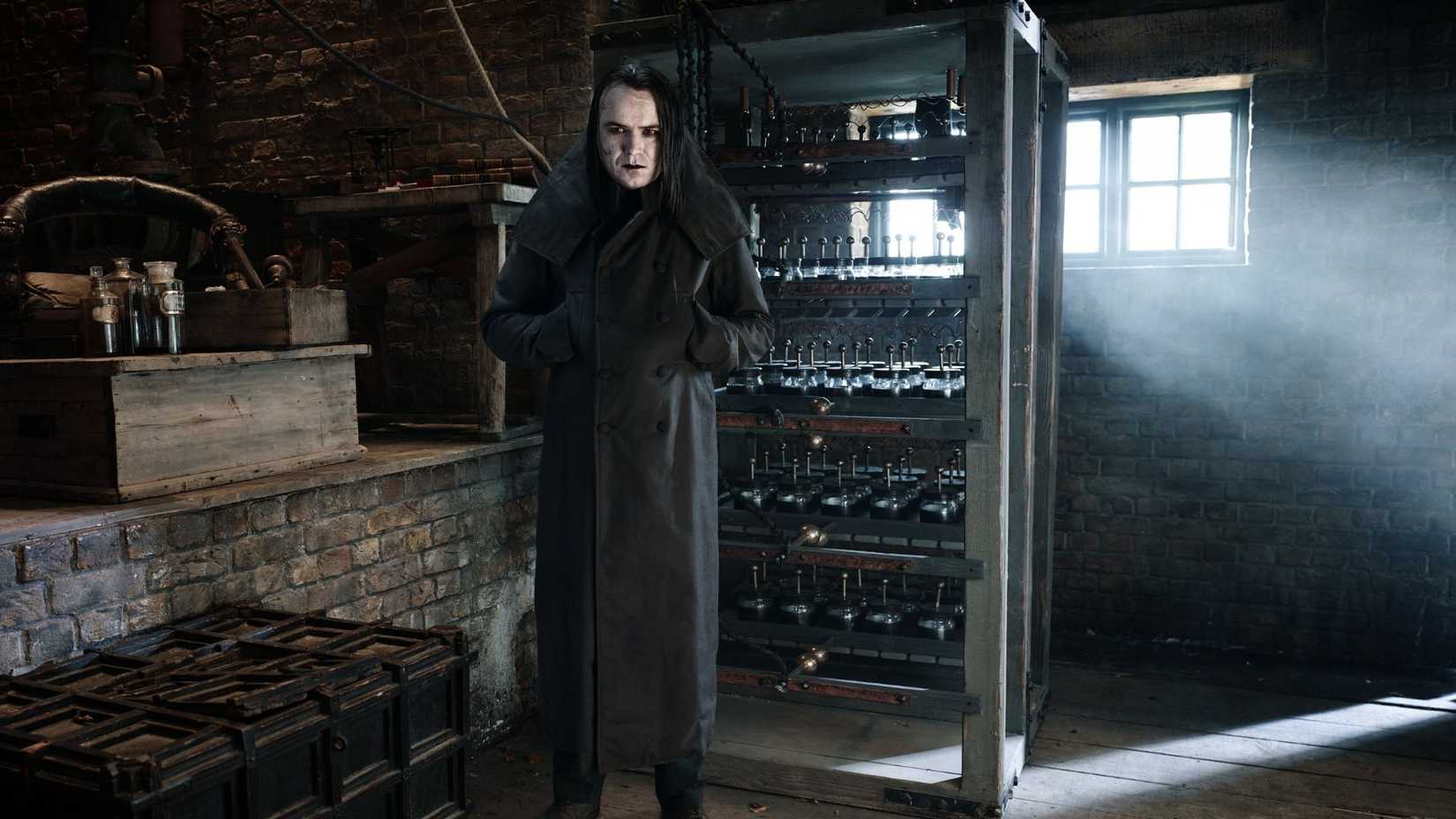 A man playing Frankenstein is dressed all in black and standing in a Victorian-era basement