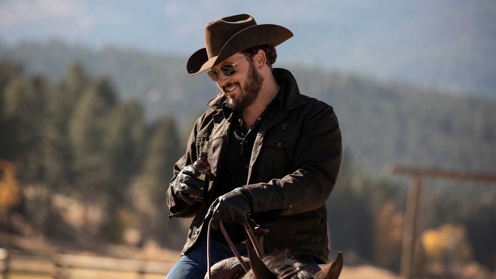Cole Hauser as Rip Wheeler, smiling and wearing sunglasses while on horseback