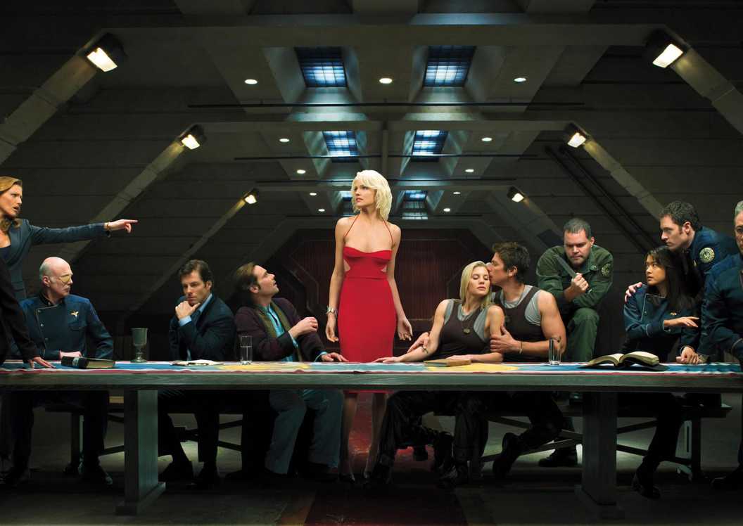 The main cast of Battlestar Galactica sitting at a table with Number 6 in the middle