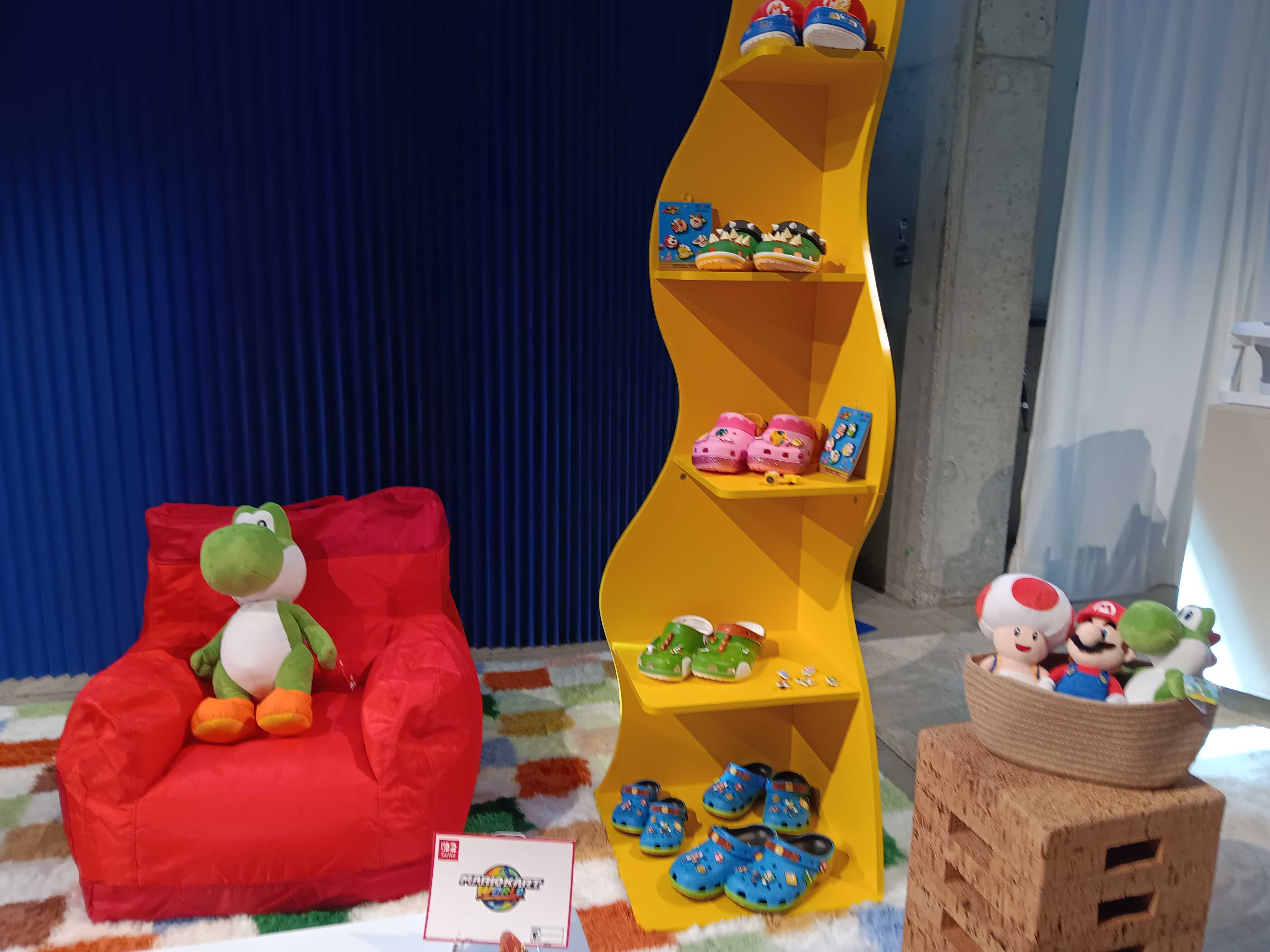 Nintendo Crocs on a yellow shelf with Yoshi plushie on a red chair and other mario plushies in a bucket