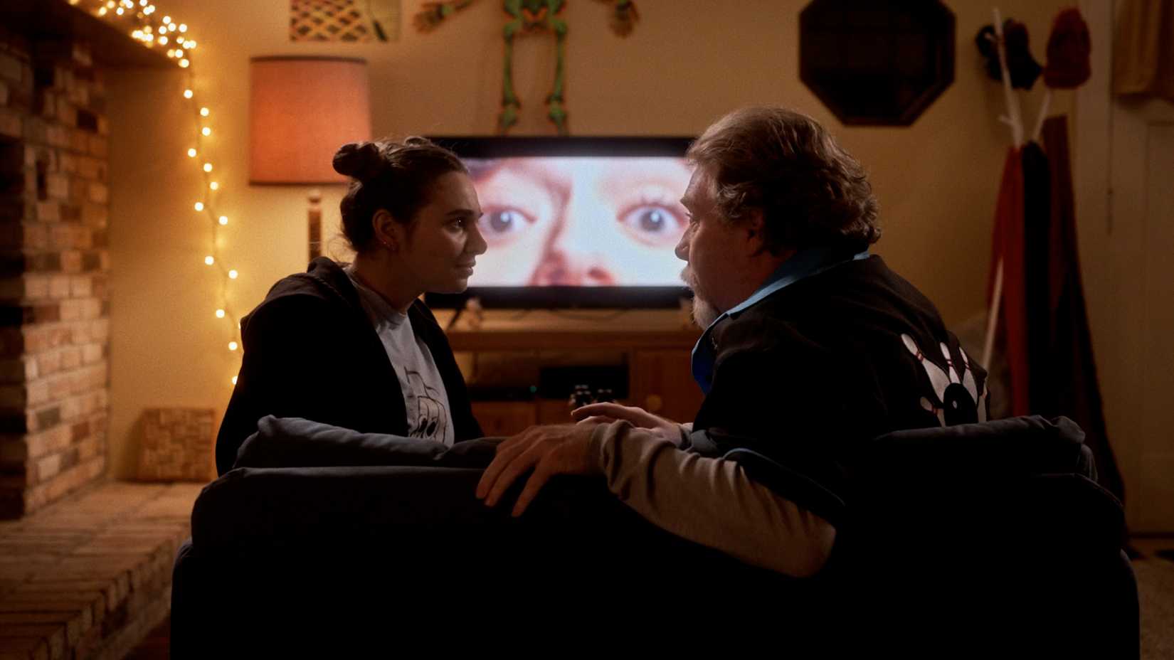 A woman and her uncle sit on a sofa watching a horror movie in Dead Media (2026)