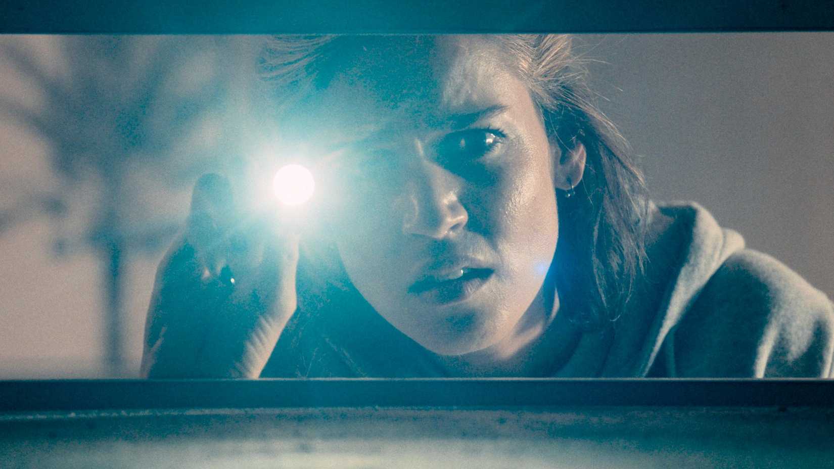 A woman shines a light into an air vent in Crawlers (2026)