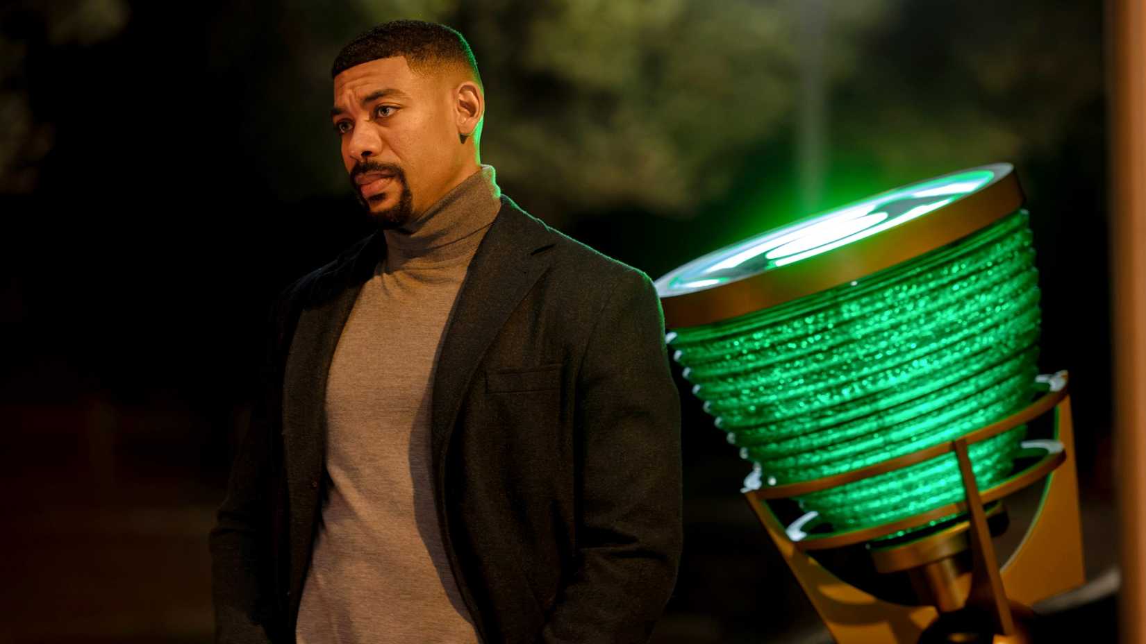 Aaron Pierre as John Stewart looking at someone with the Green Lantern signal behind him