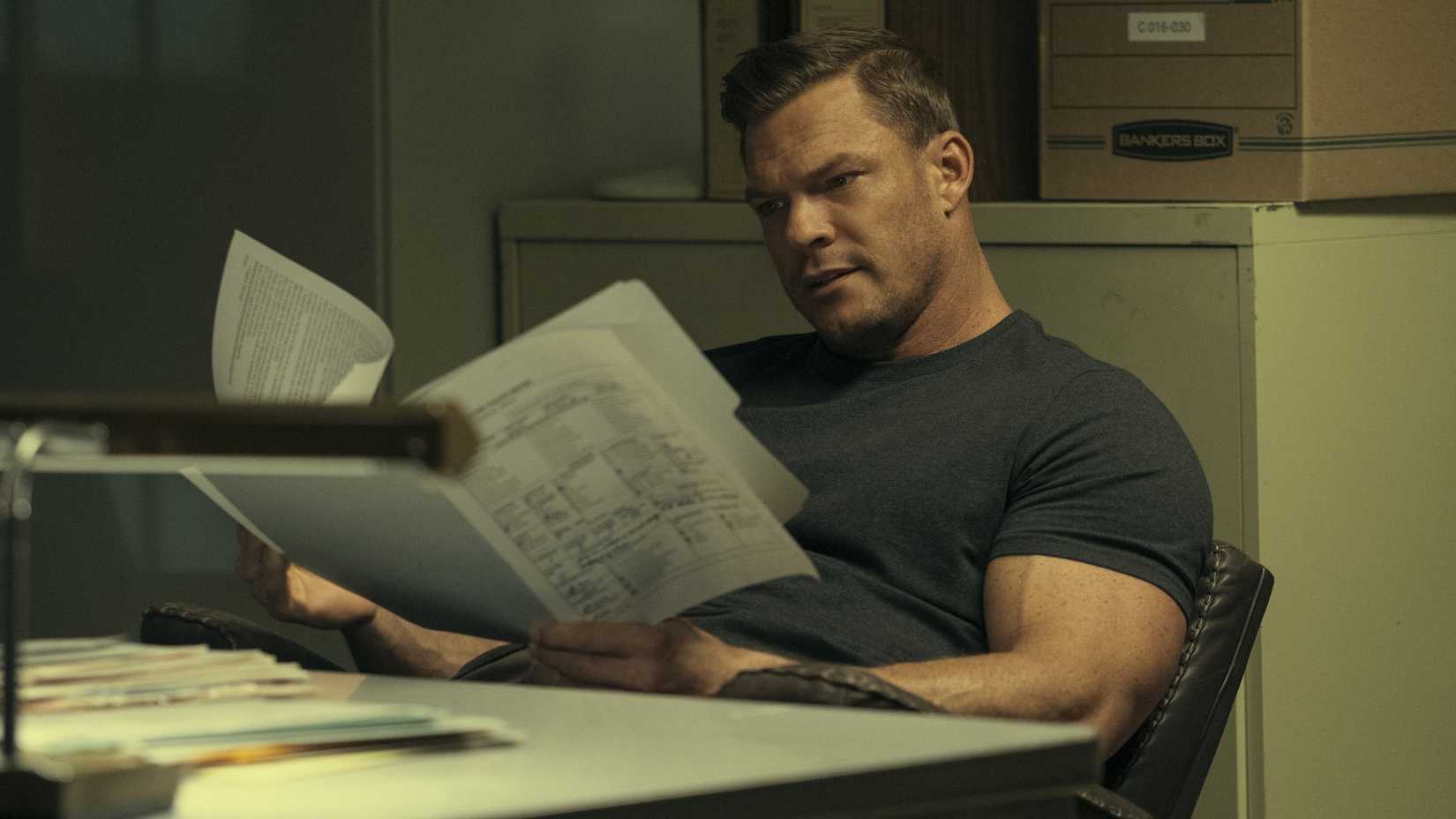Alan Ritchson as Reacher reading files at his desk in Reacher