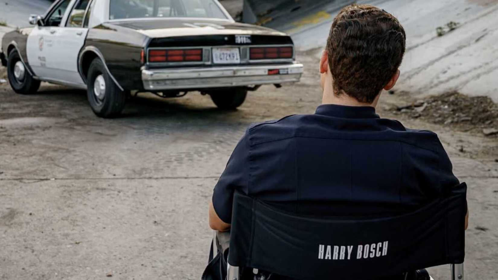 Cameron Monaghan as young Harry Bosch sitting in a chair while looking at a cop car in Bosch: Start of Watch