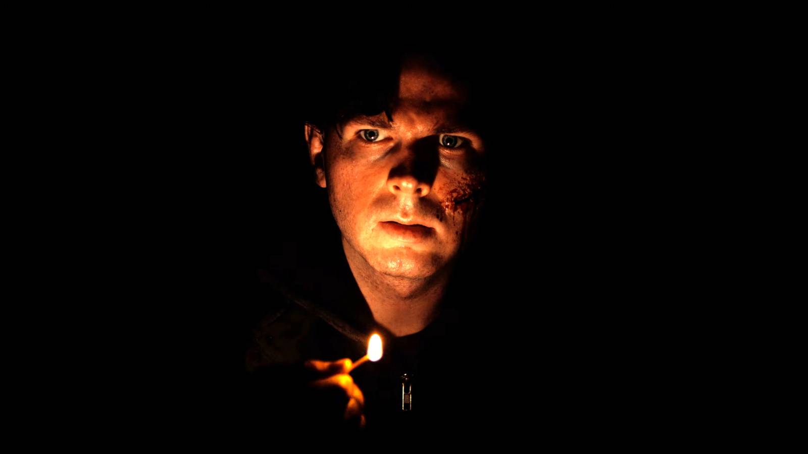 Chandler Riggs' Ethan Winters looking worried while holding a match near his face in Biohazard
