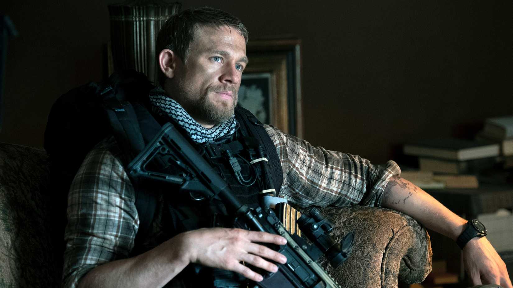 Charlie Hunnam's Ironhead sitting in a chair with his rifle on his chest in Triple Frontier