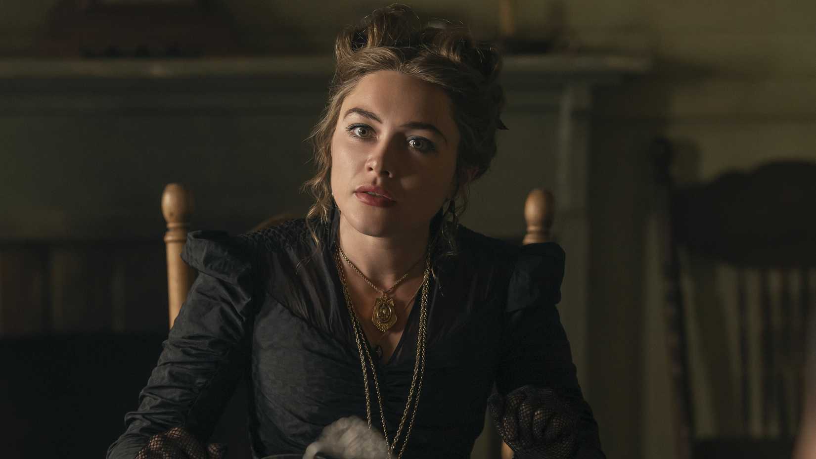 Florence Pugh as Cathy sitting at the head of a table and wearing black in East of Eden