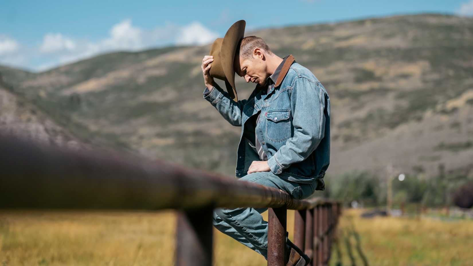 Jefferson White's Jimmy with his head down and taking off his hat while sitting on a fence in Marshals season 2