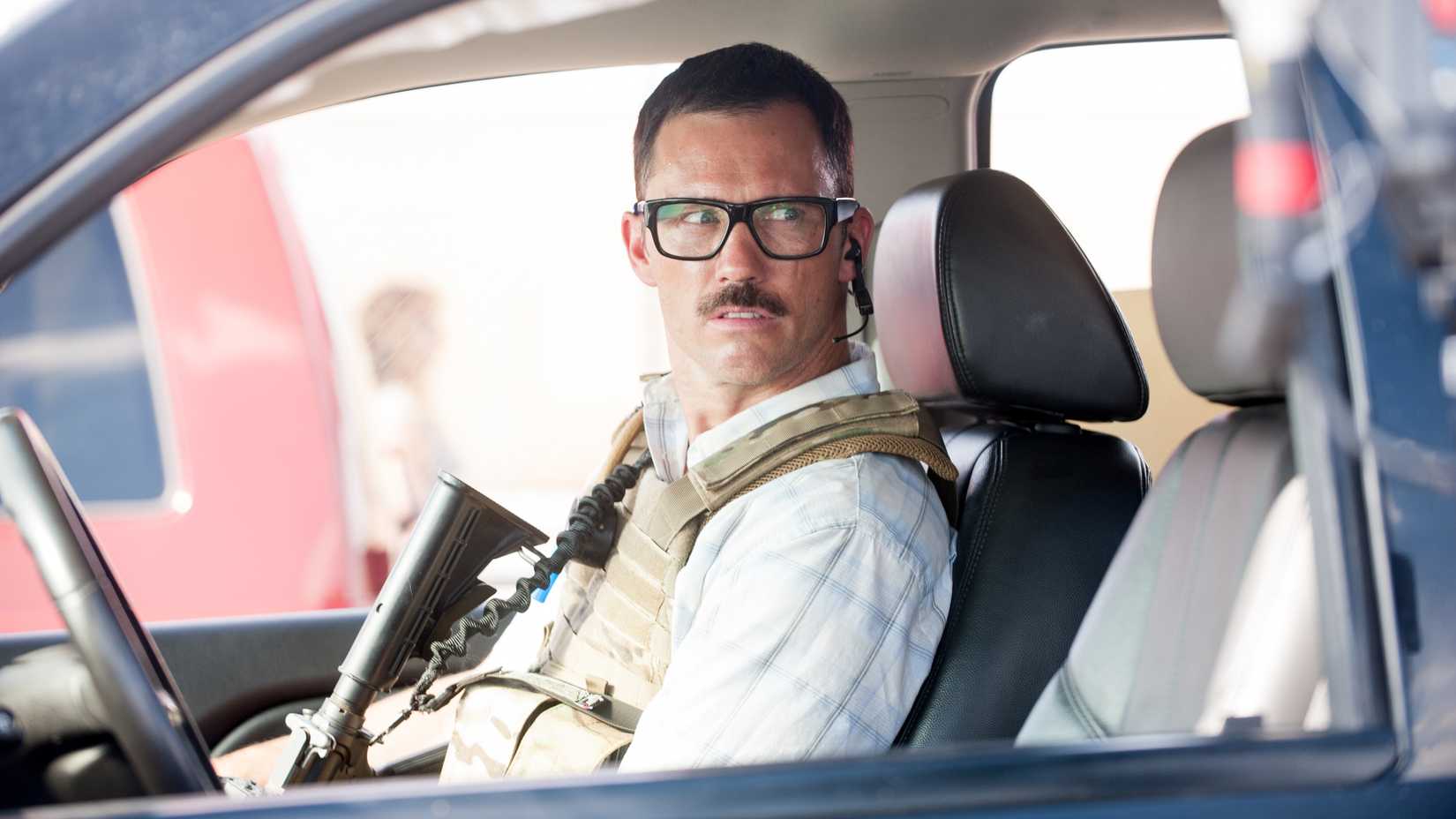 Jeffrey Donovan como Steve segurando um rifle e olhando intensamente sentado no banco do passageiro em Sicario