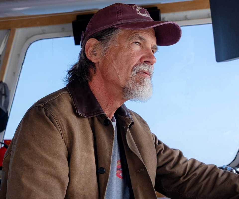 Josh Brolin driving a boat and wearing a maroon hat in Whalefall