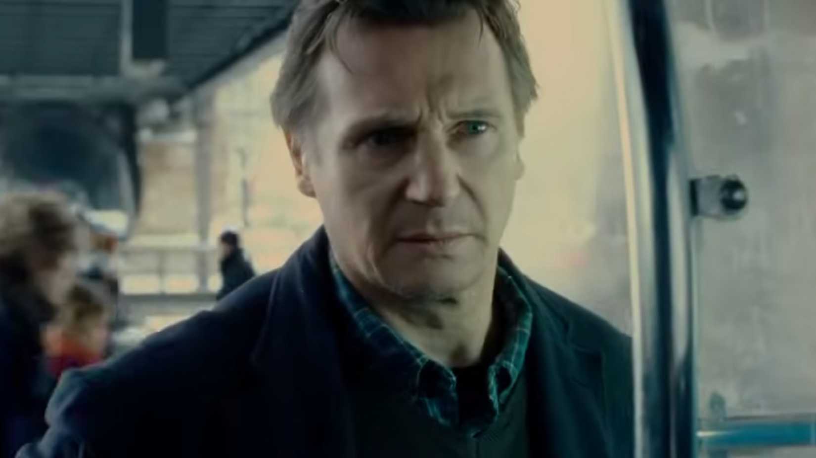 Liam Neeson looking serious by a phone booth in unknown