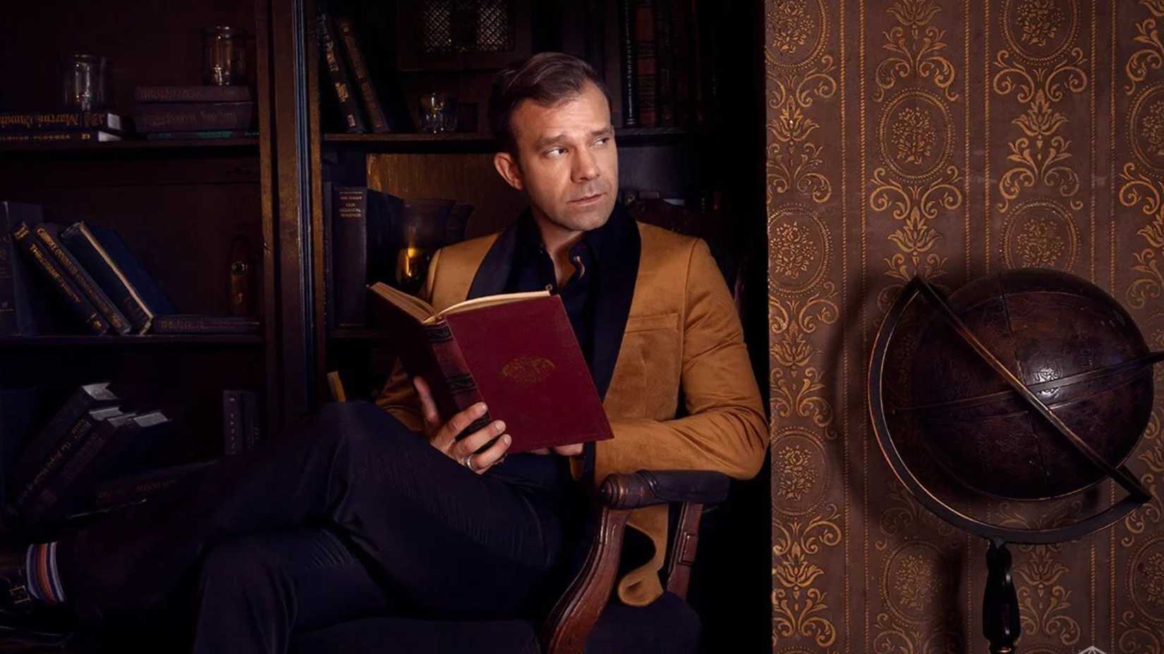 Liam O'Brien from Critical Role holding a book and looking to the side