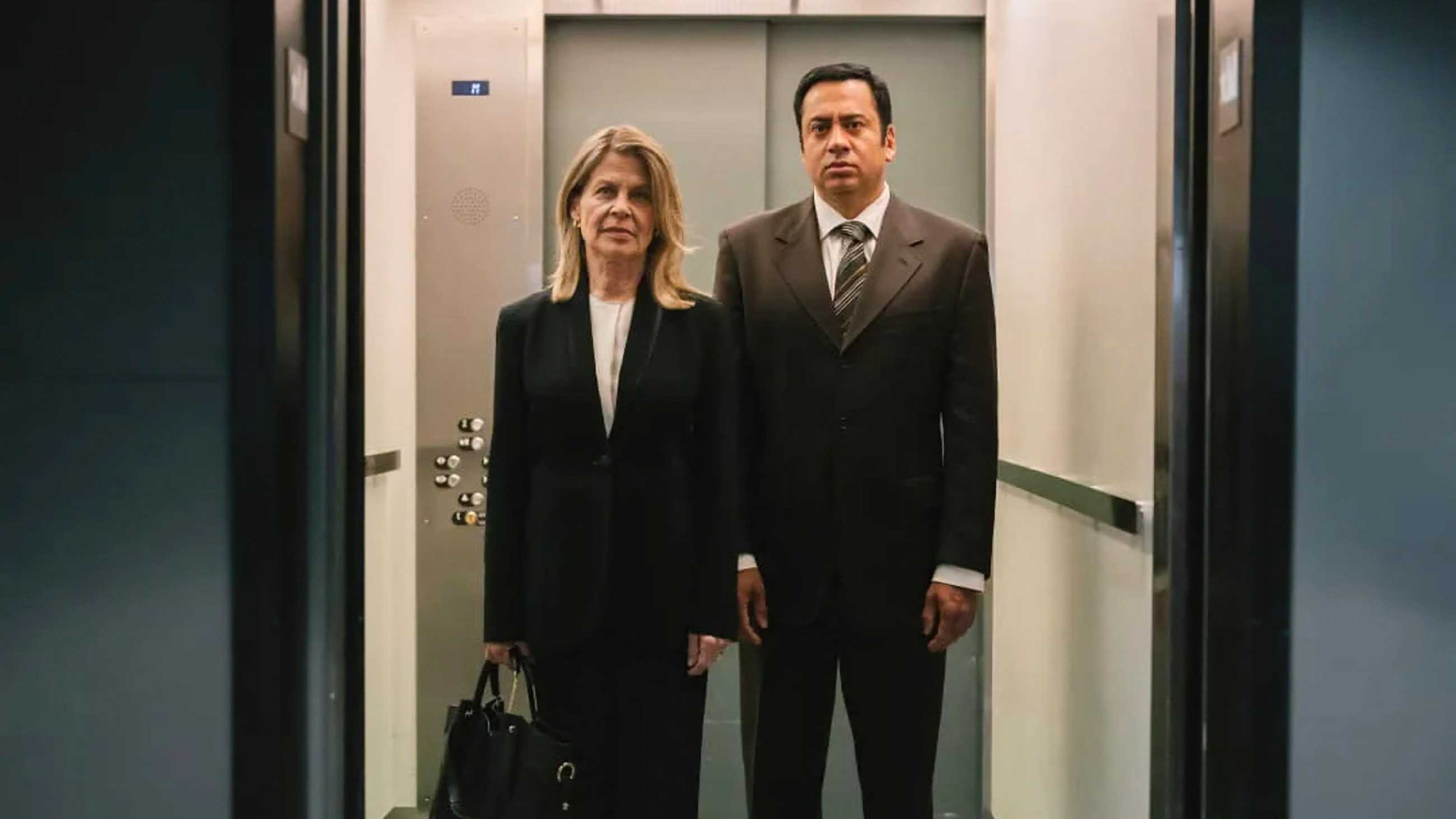 Linda Hamilton and Kal Penn in black suits in an elevator in Trust Me, I'm a Doctor