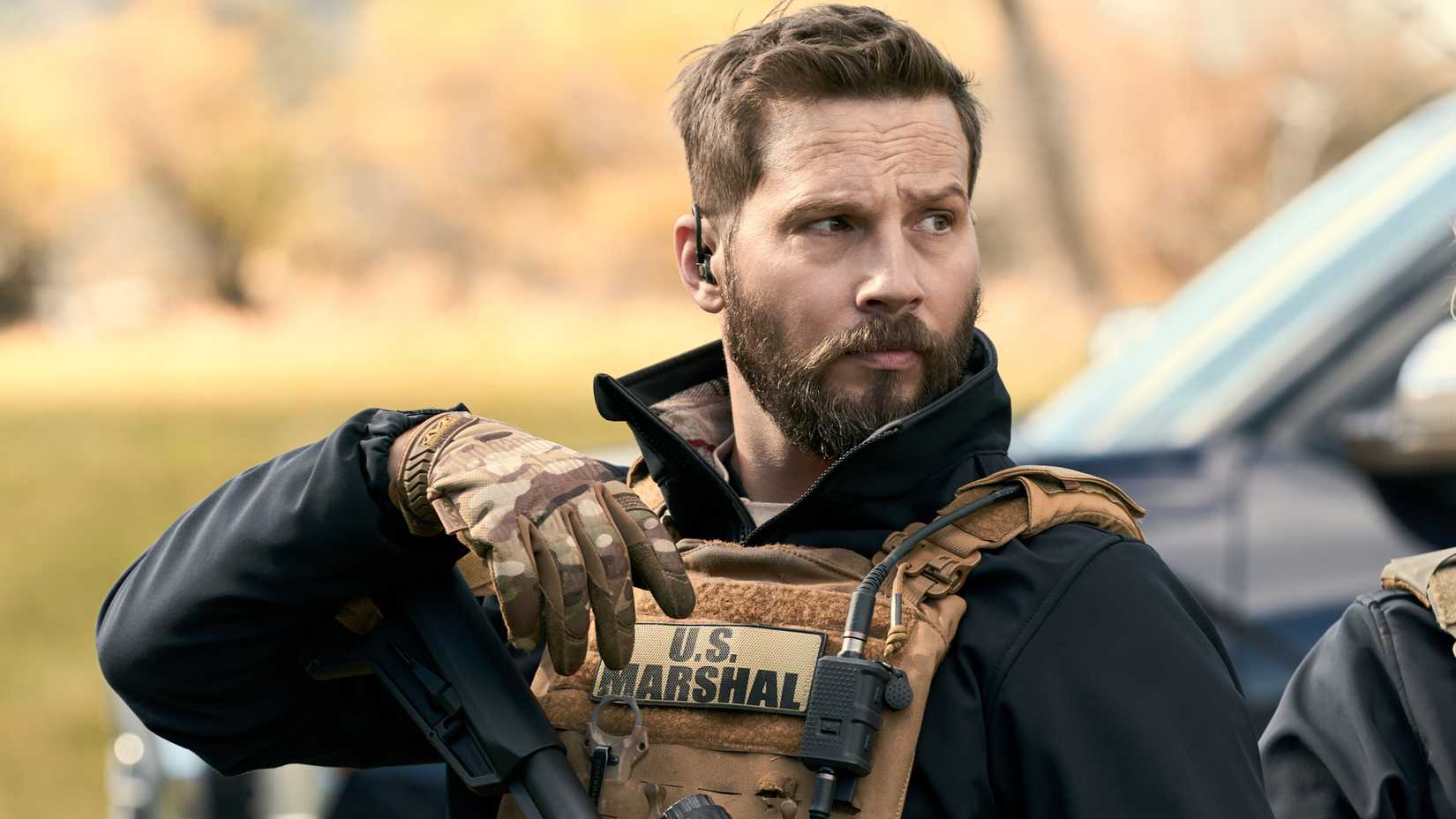 Logan Marshall-Green's Cal looking curiously in his tactical gear and his arm resting on the butt of his rifle in Marshals season 2