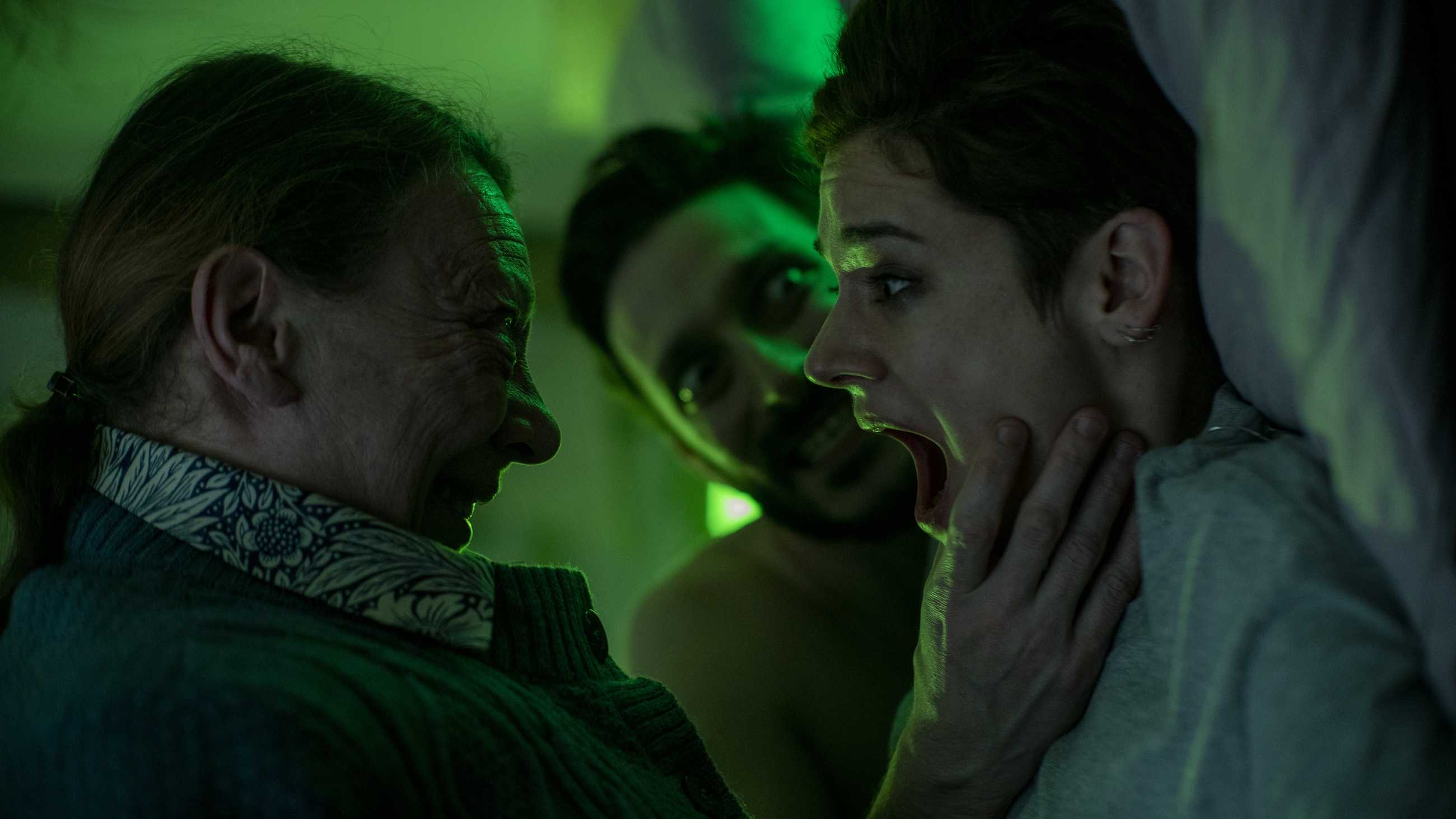 The witch grabs Emma Larsimon's face while a man next to her has bulging eyes and an evil smile in Marianne