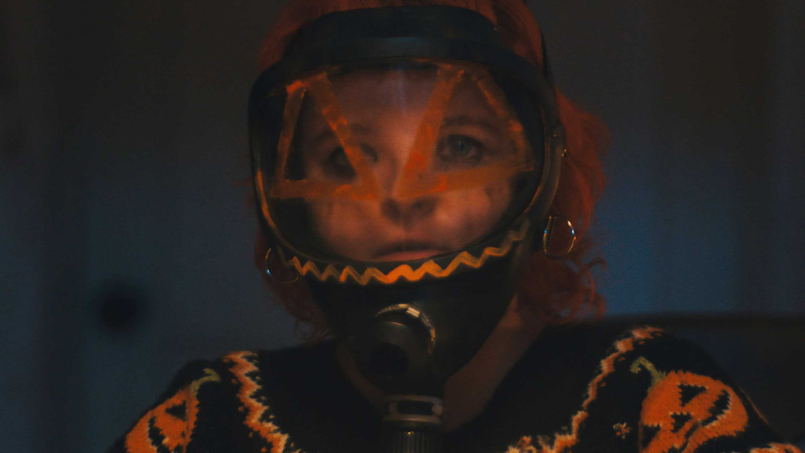 Milly Shapiro as Pumpkin in a gas mask painted like a jack-o'-lantern in Hallowarrior