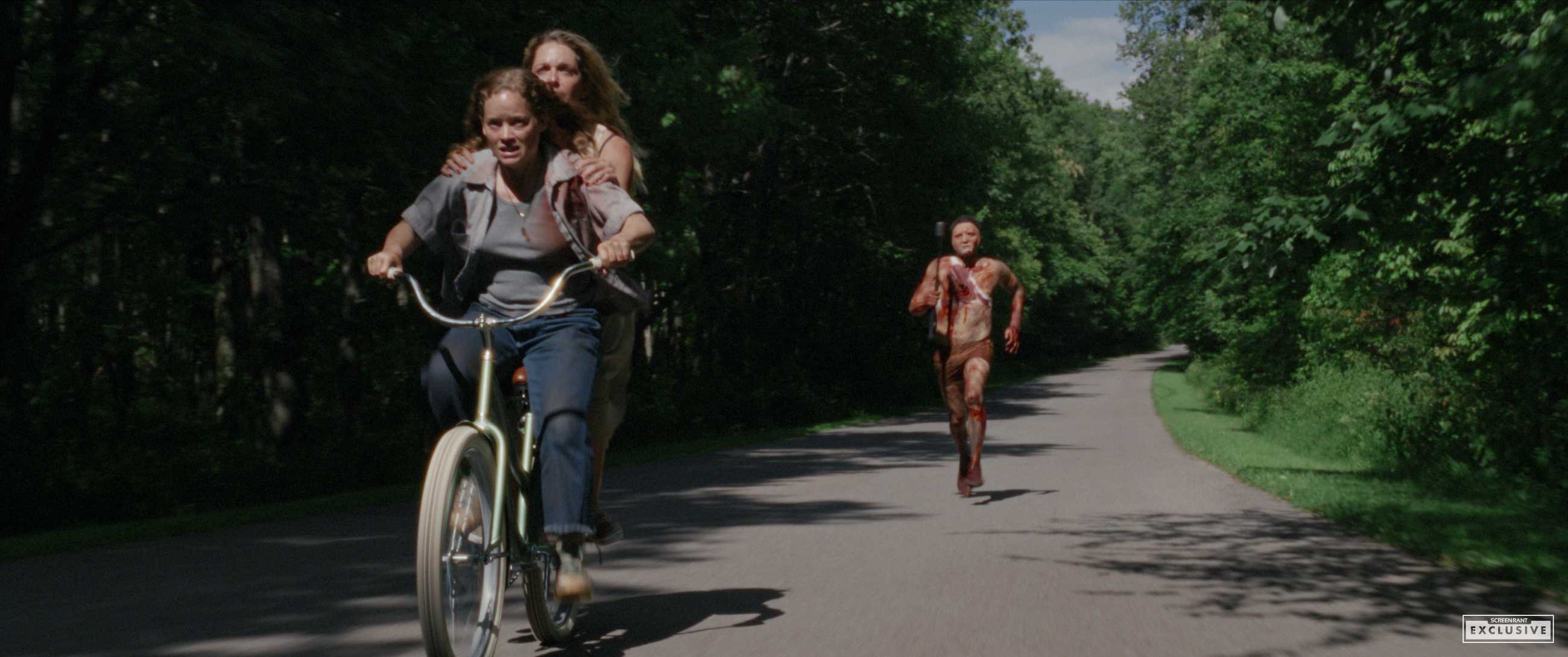Two women on a bicycle being chased by a bloodied, masked killer in River