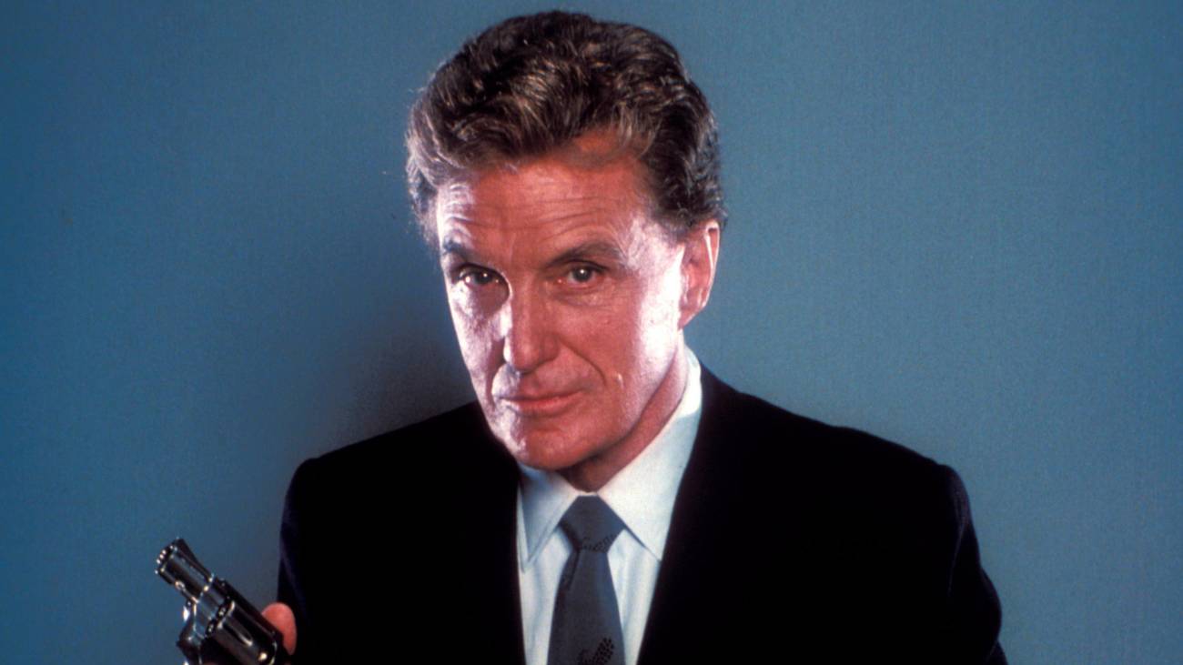 Robert Stack, the host of Unsolved Mysteries, holds a gun
