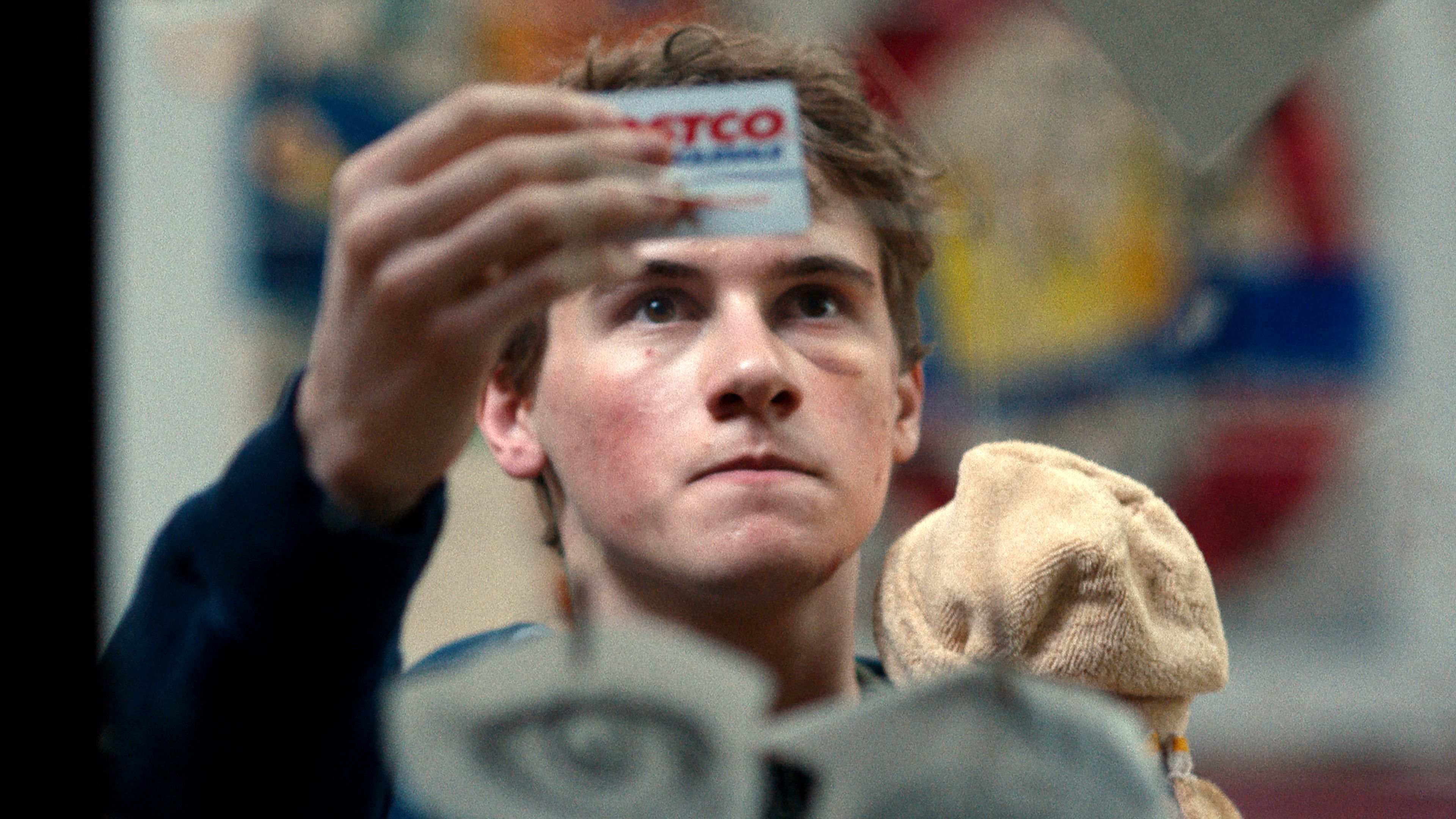 sam-nivola-s-sonny-looking-intently-while-holding-up-a-costco-card-in-phony Phony: Hulu’s New Mystery Series Is An Instantly Gripping & Enjoyable Ride | Review