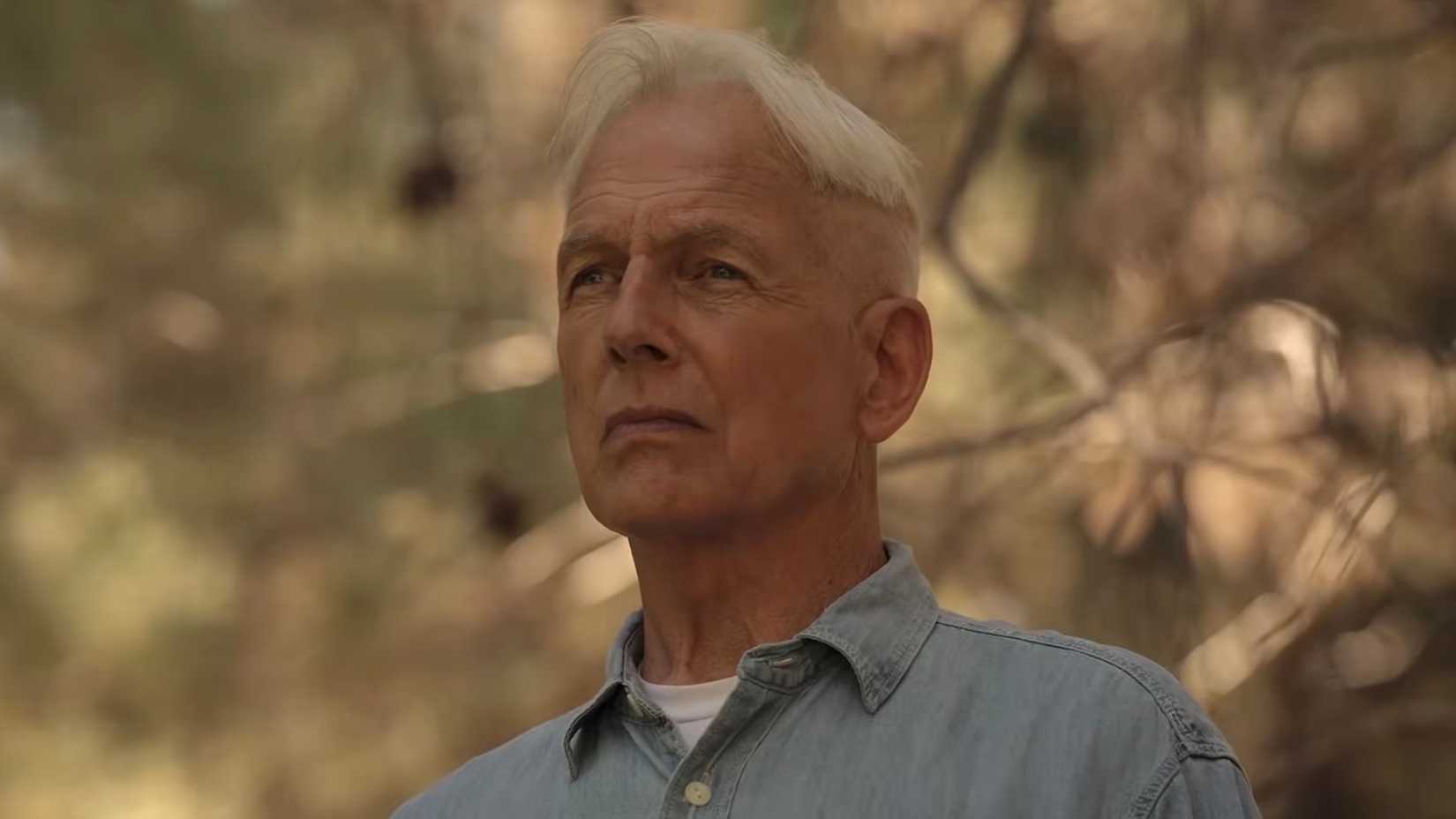The older Gibbs standing outside of his Alaskan cabin