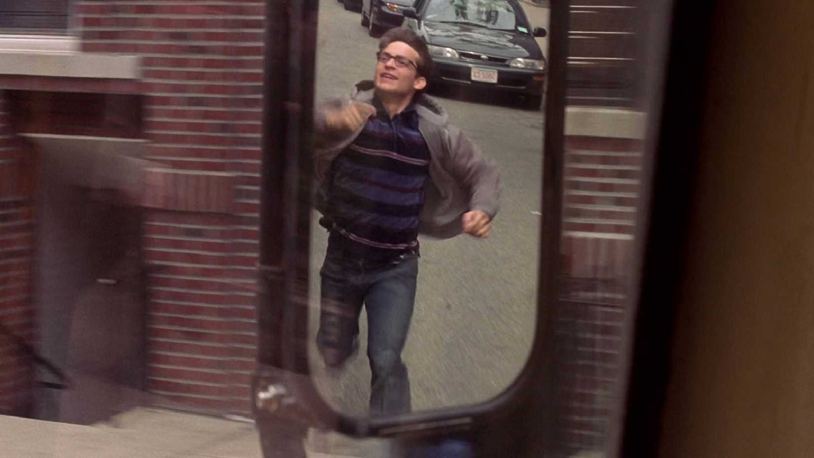 Tobey Maguire como Peter Parker correndo ao lado de ônibus em Spider-Man (2002)
