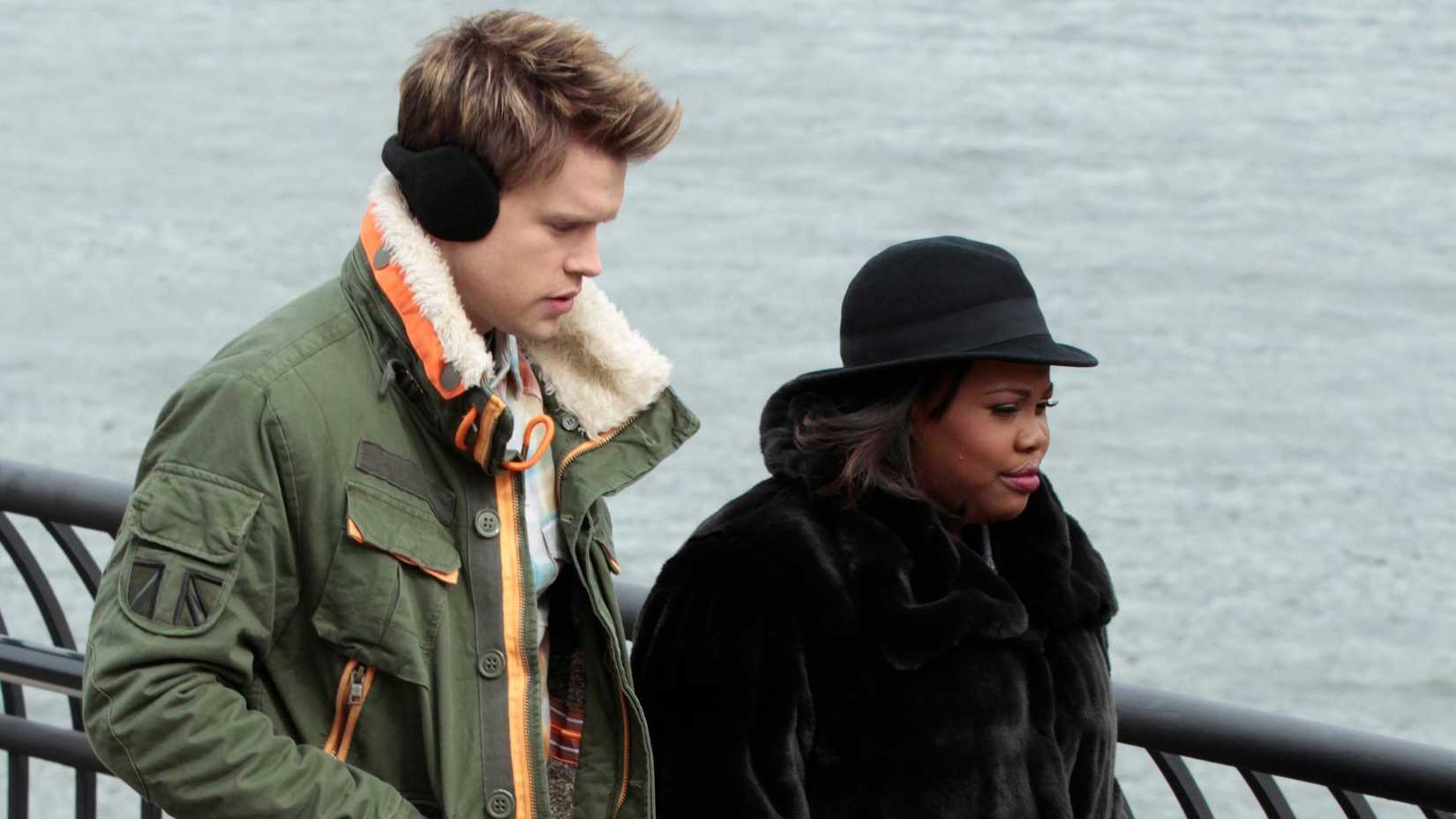 A young white man and a young Black woman bundled up in winter clothes walking down a street