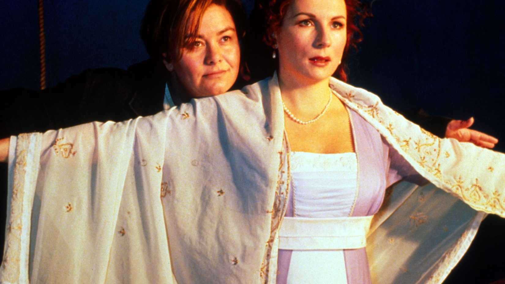 A woman stands behind another woman who is spreading her arms wide