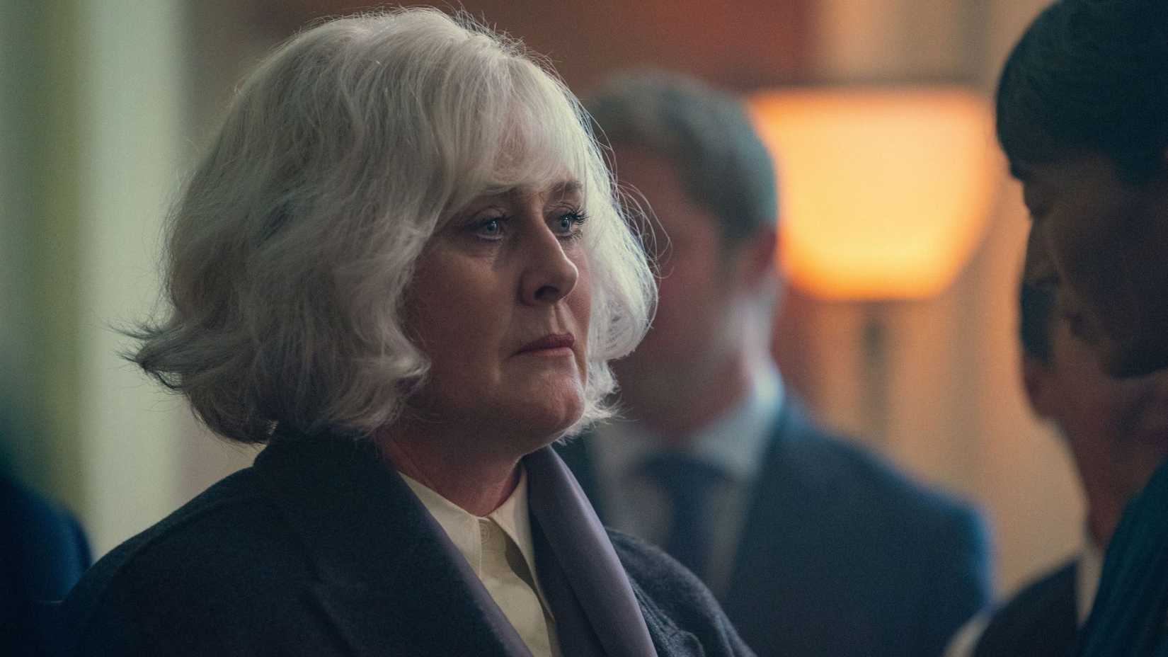 A woman with white hair stands in a room of people