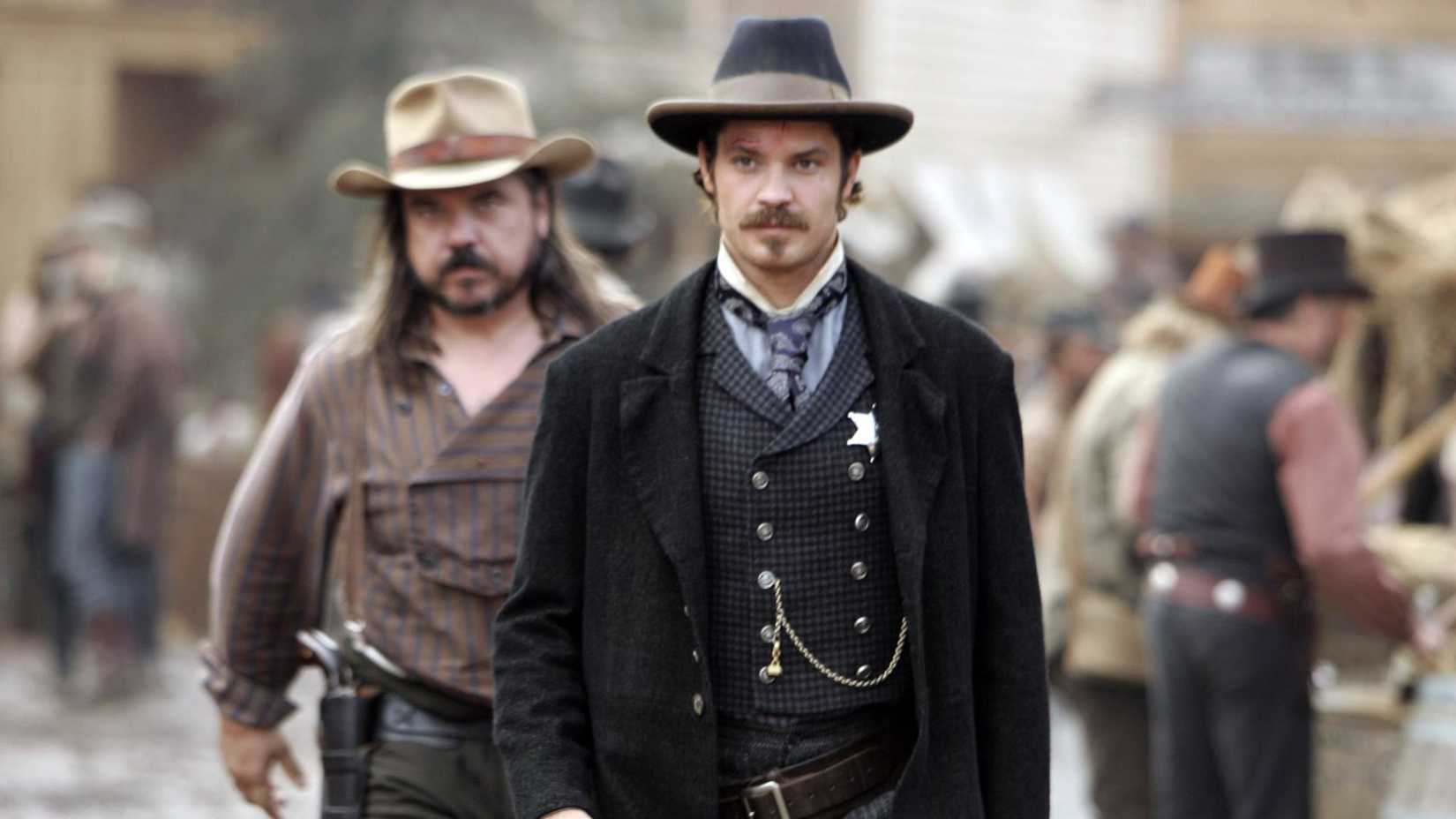 Two men dressed like they live in the Old West walk, one man is wearing a Sheriff badge