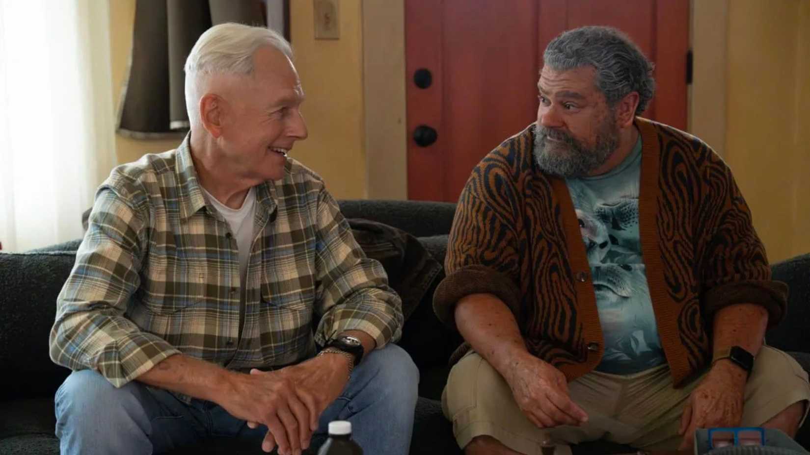 Two older men sit on a couch talking