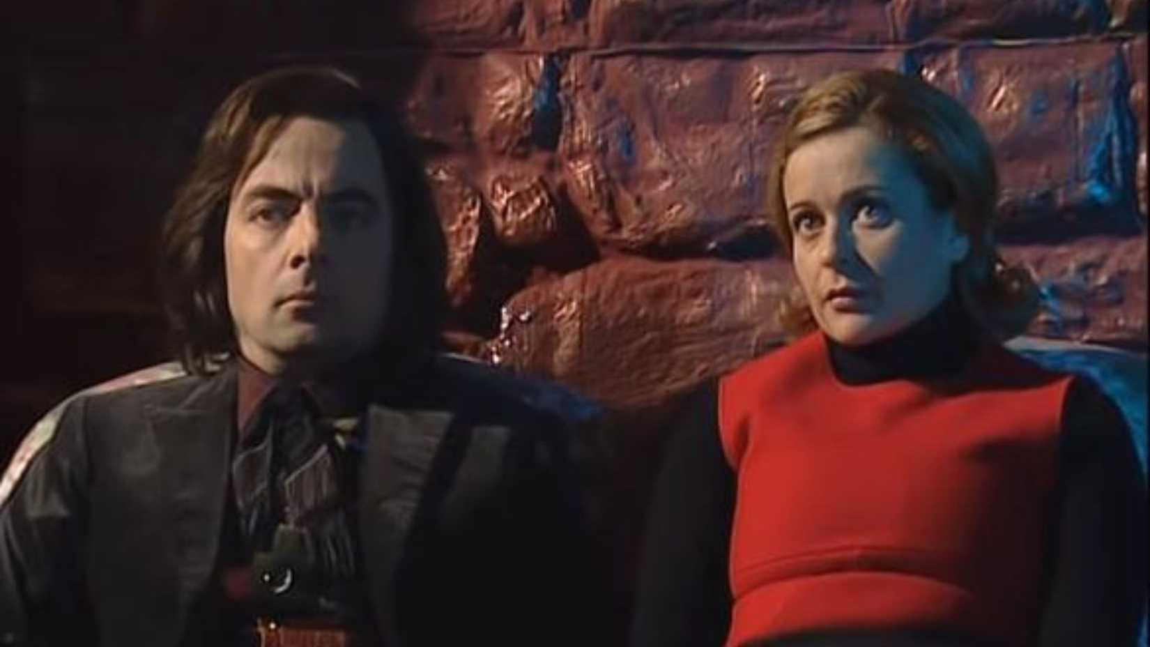 A man and woman sit against a stone wall