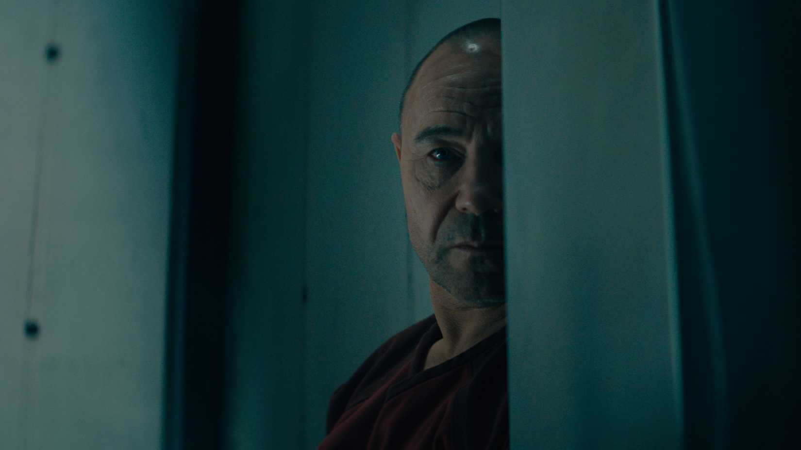 Yurek Walter's face is half blocked by a cell wall in Nocturne