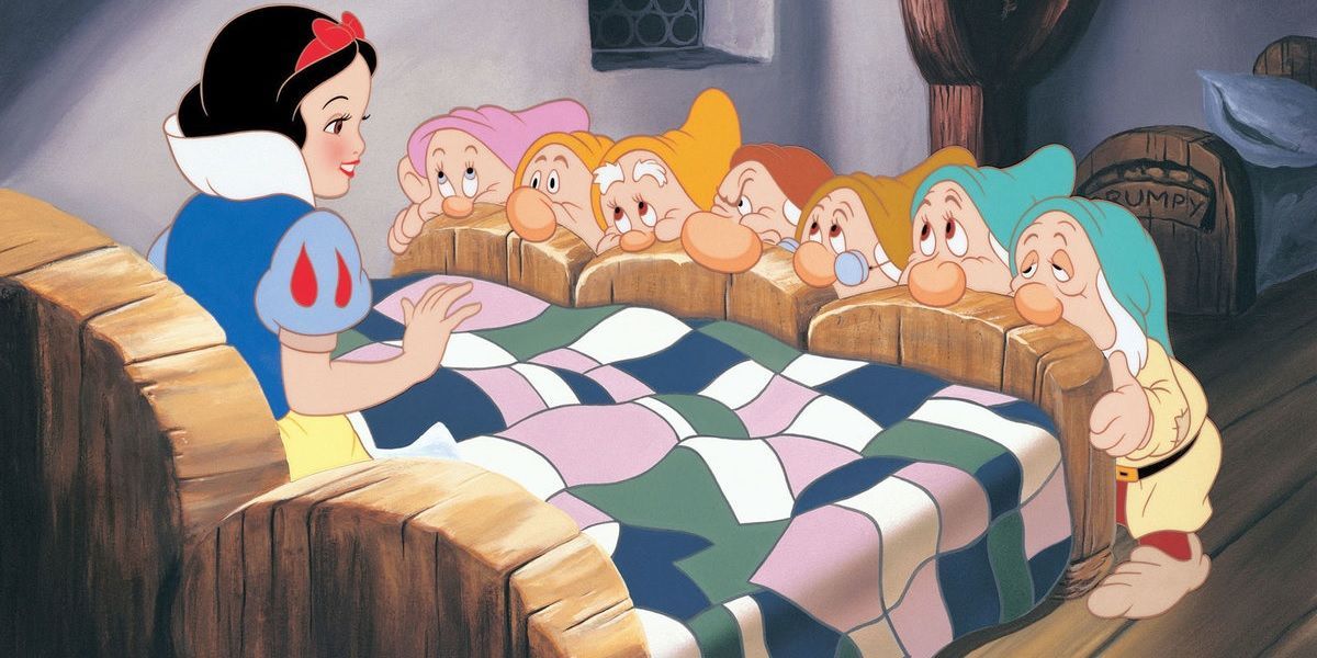 The seven dwarfs stand at the foot of the bed where Snow White sits in the Disney animated movie.