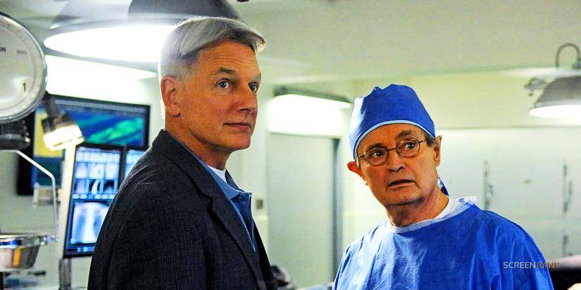 Leroy Jethro Gibbs and Dr. Donald "Ducky" Mallard, wearing scrubs, look alert in the medical examination room